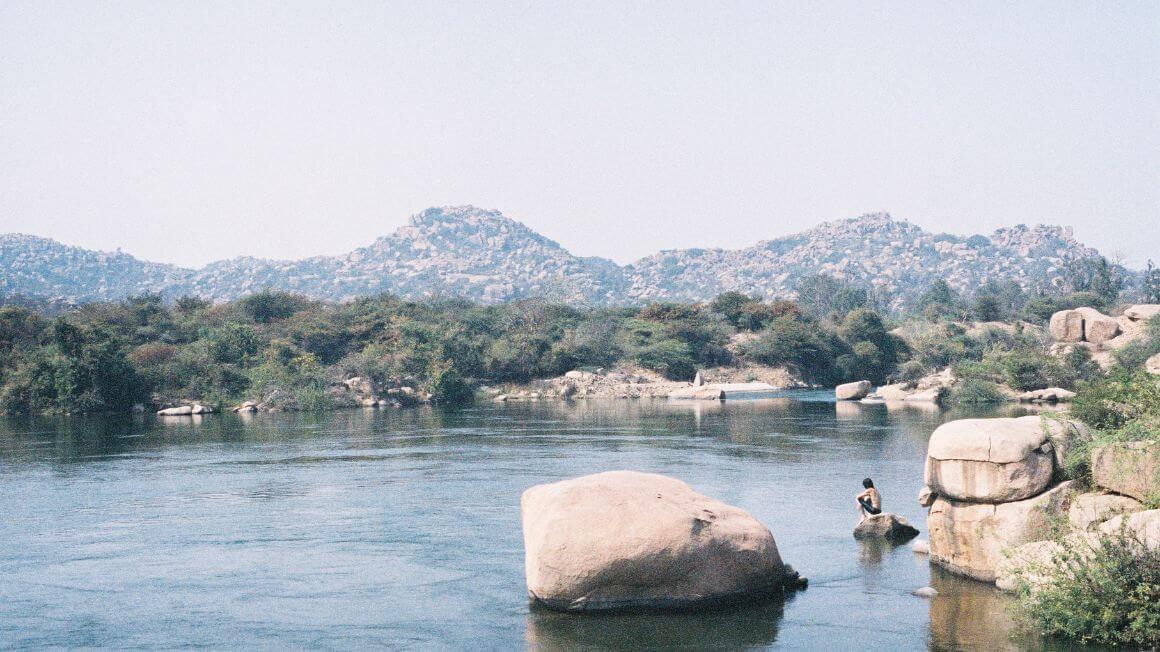 a man sits on top of a rock by the river in hampi, india