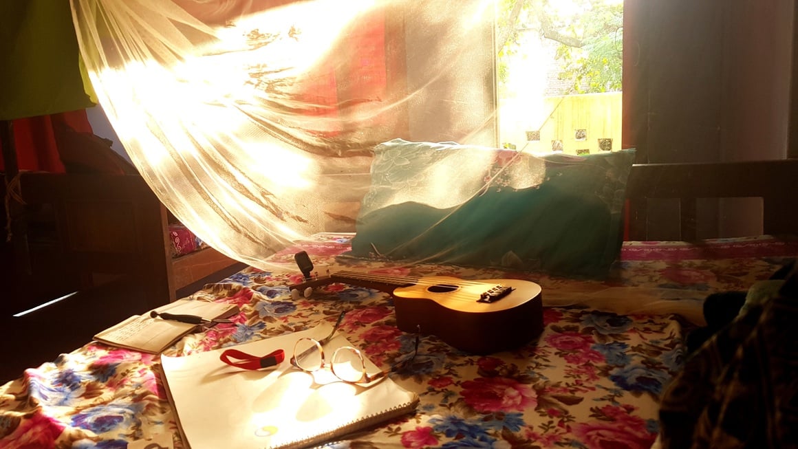 Ukulele and notebook on a bed with sun shining through the mosquito net hanging above it