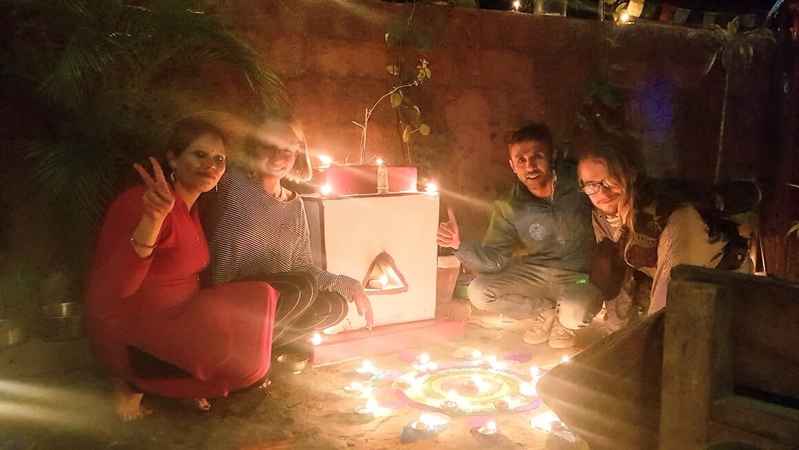 pair of backpackers smiling with guesthouse owners in Nepali in front of lit Rangoli Tihar display