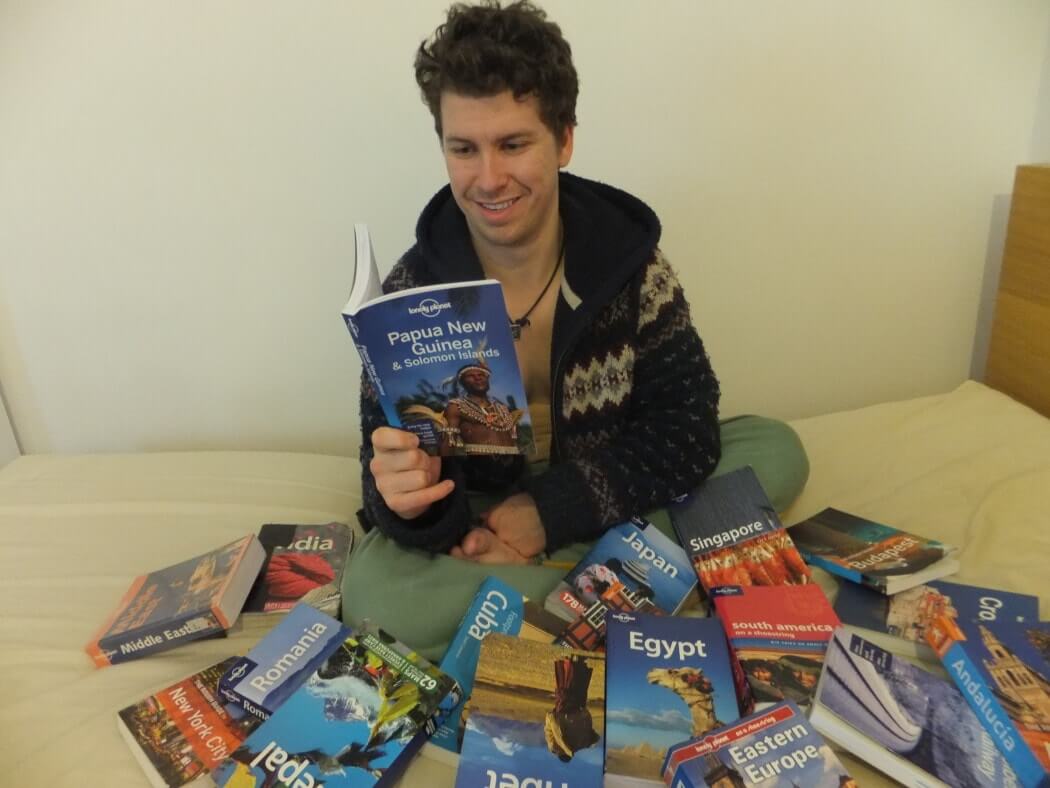 man surrounded by lonely planet travel guides while reading one about papua new guinea