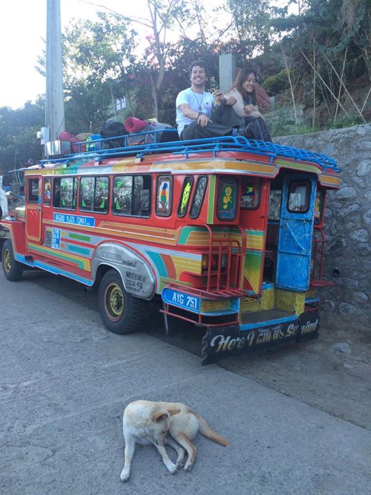 Two people sat on top of a colourful public jeepney bus