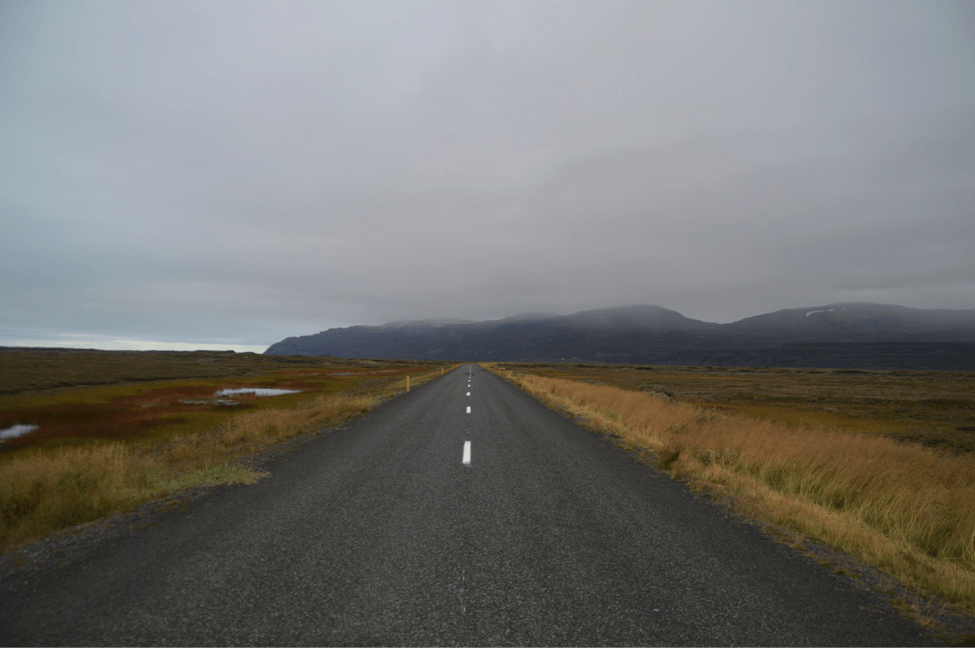 Driving down a remote road with mountains in the distance in Iceland