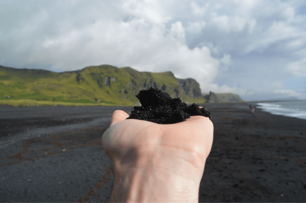 A person holds up a handful of black sand from a volcanic beach in Iceland