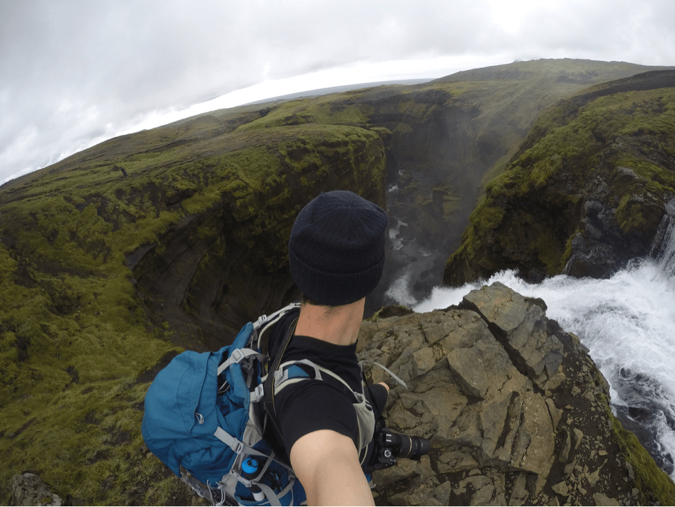 A person takes a selfie on a GoPro next to the top of a massive waterfall in Iceland