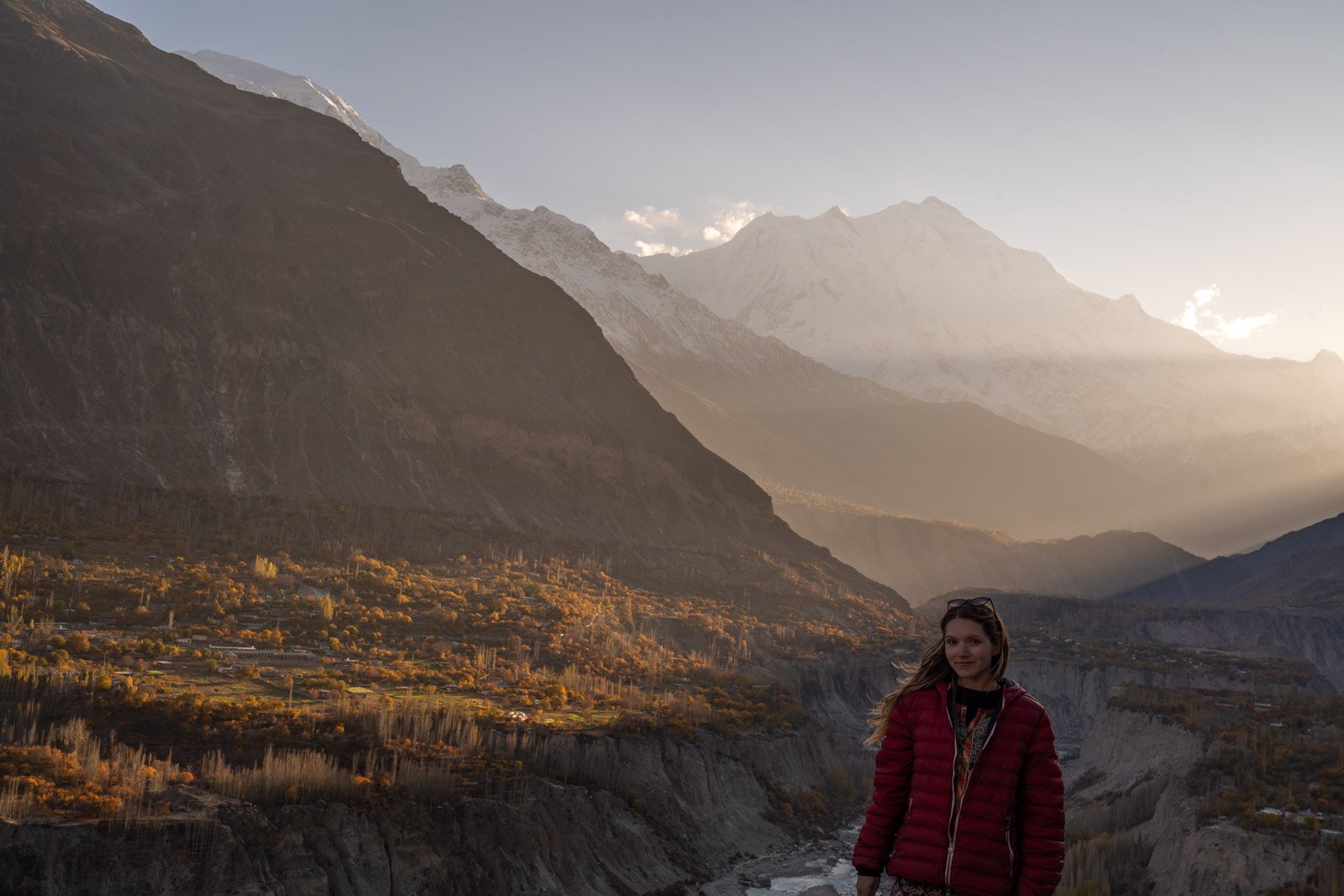 girl in red jacket standing in front of a mountain in hunza valley pakistan