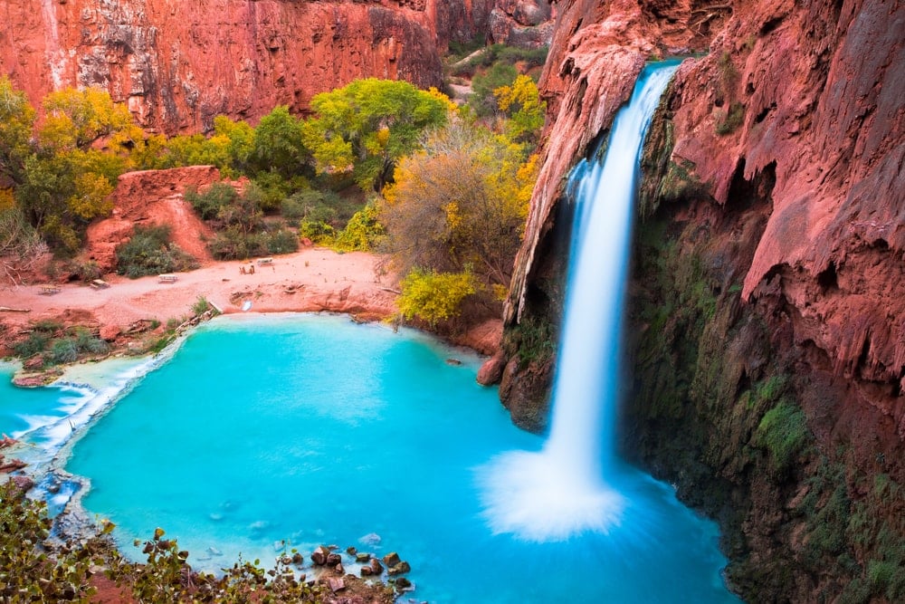 a water fall tumbling into a bright blue pool surrounded by reddish mountains in the USA