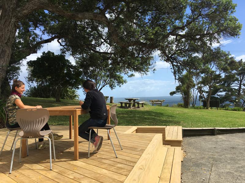 Waiheke Backpackers Hostel best hostels in Auckland overlooking the ocean with seating area under the trees