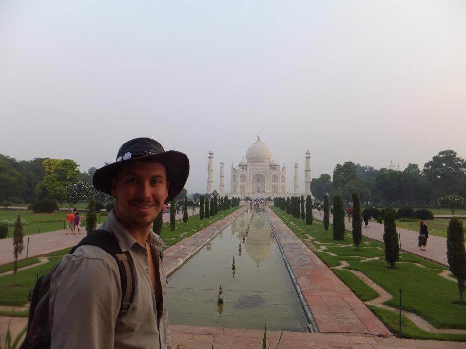 young will standing in front of the taj mahal wearing a black bucket hat in india
