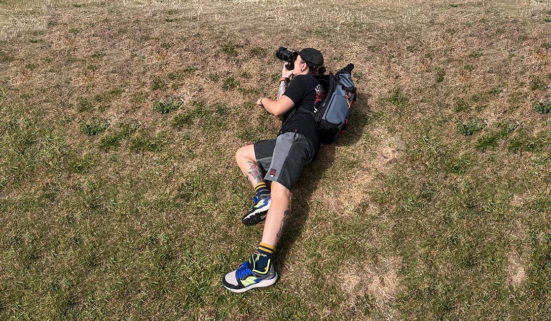 Nic laid on the floor taking a photo wearing the Wandrd Prvke backpack