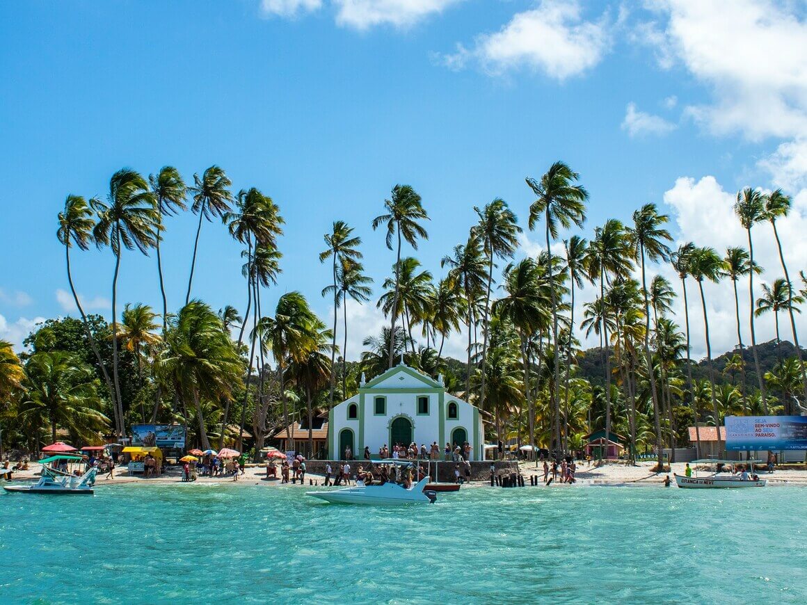 Crystal clear water and in the background an old colonial house surrounded by palm trees and white sand.