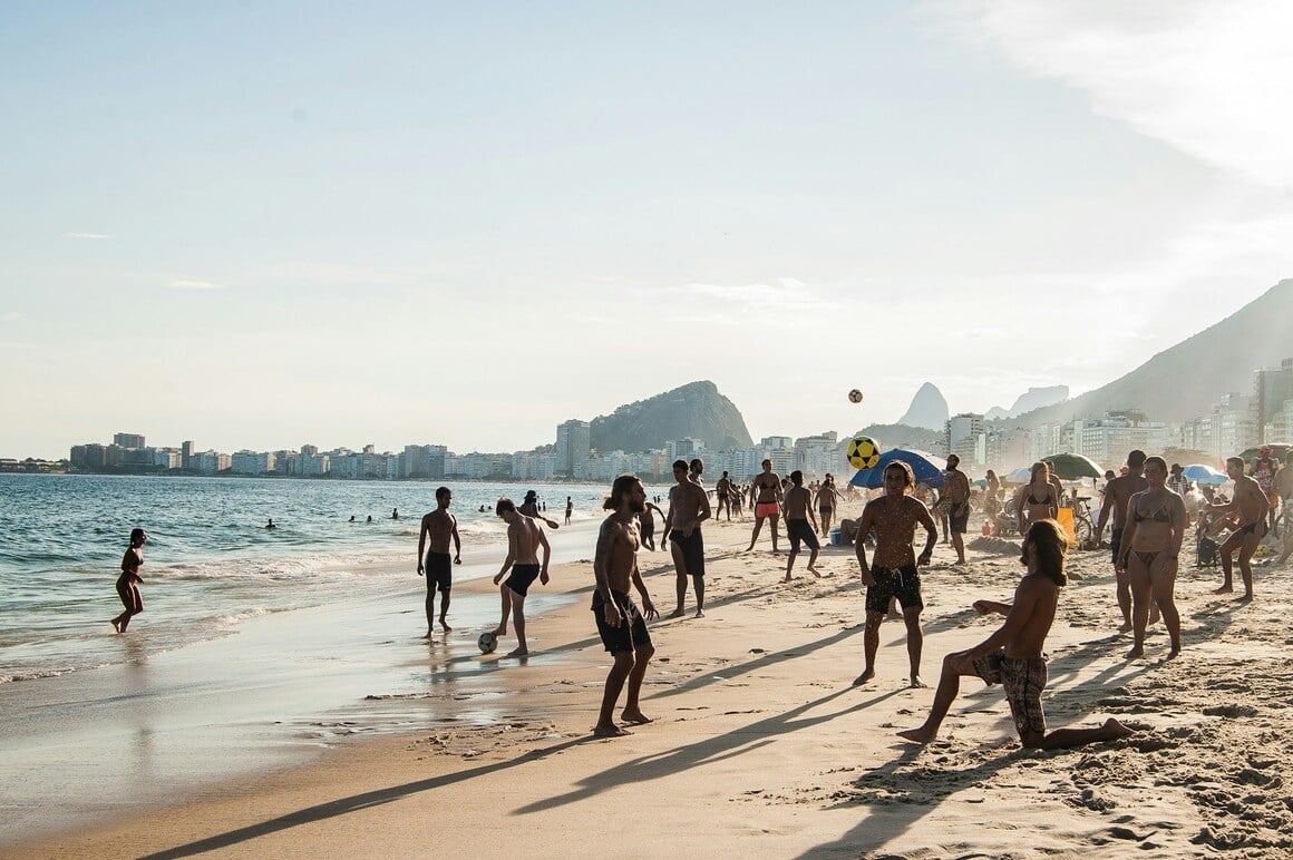 People playing soccer and other sports on the beach by the sea at sunset.