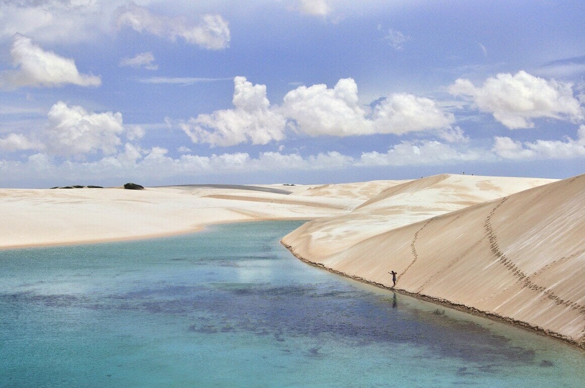 
A person walking downhill on a sand dune in a large desert with water surfaces scattered along the dunes.
