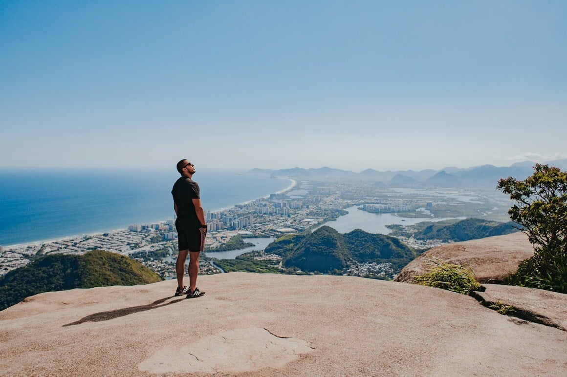 A young person looking at the sky on a sunny day from a viewpoint and in the background the city of Rio de Janeiro, mountains and the beach.