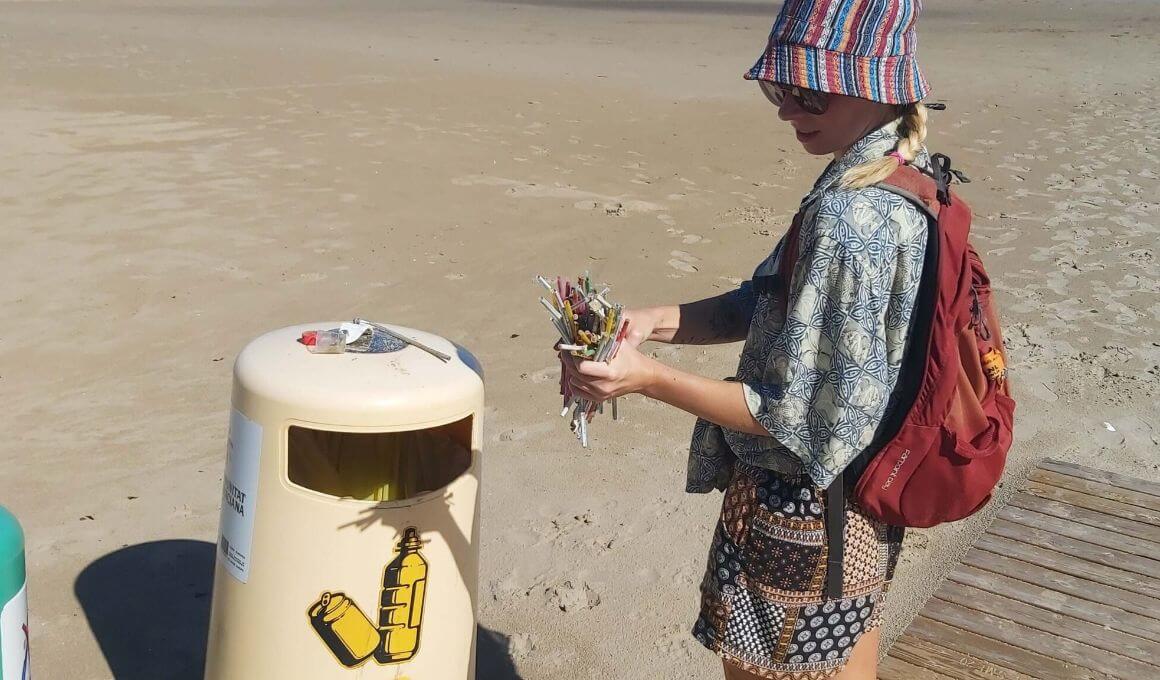 girl cleaning up a beach in spain by throwing out trash into a trash can