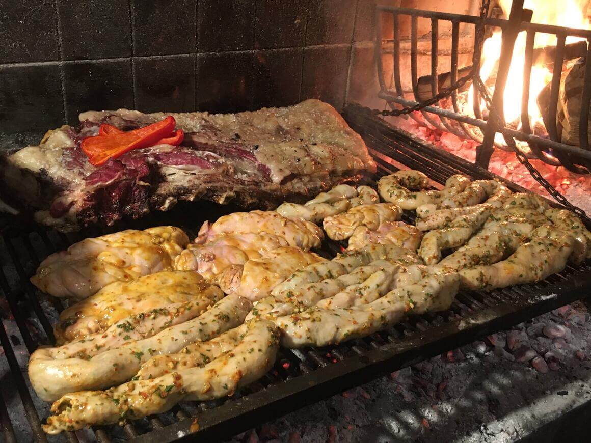 Asado parrilla grill covered in various beef meat cuts with fire burning to the side