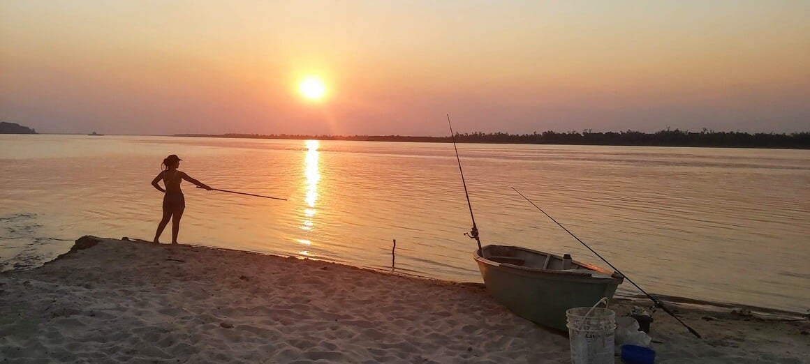 Silhouette of a woman fishing in a river in front of a red-orange sunset