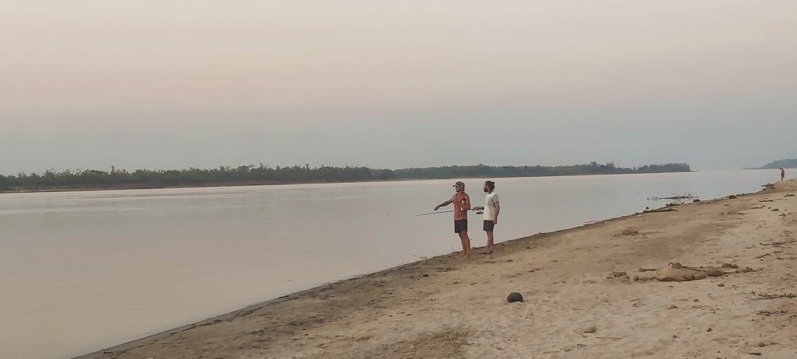 two people stood on the sandy banks of a river