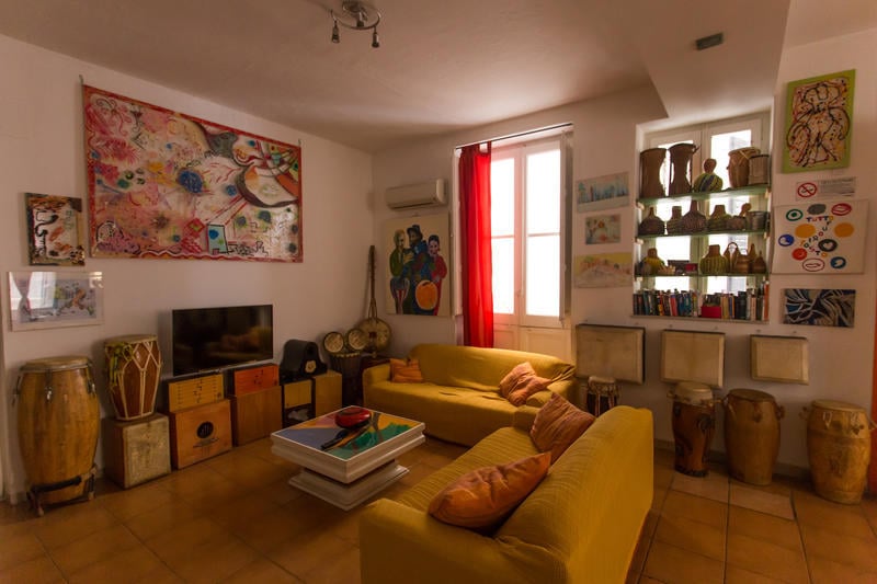 A Casa di Amici Boutique Hostel best hostels in Palermo, with a cosy yellow couch facing a tv with drums around the room for musical jams.