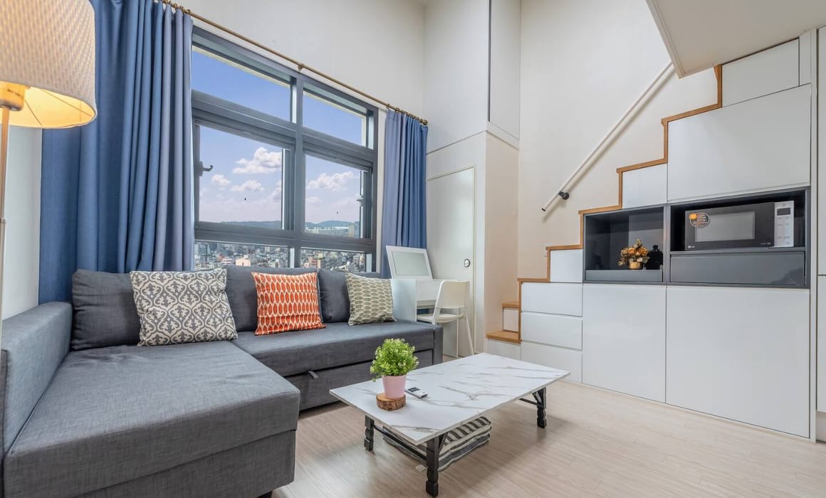 Modern Airbnb with blue curtains, gray sectional couch, and clean design