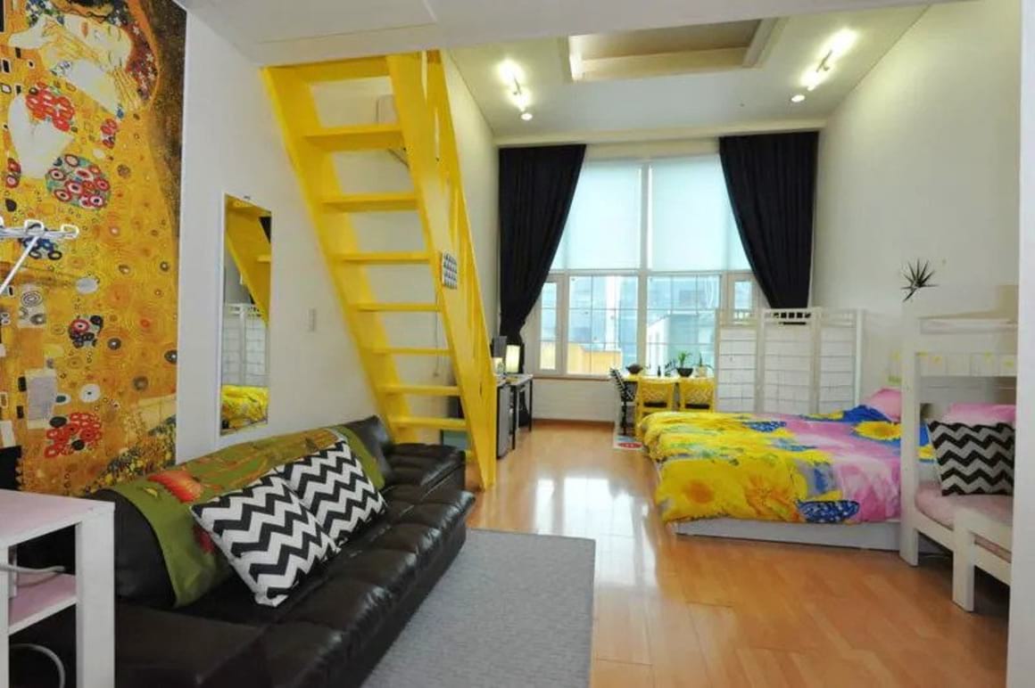 Modern designed Hongdae Guesthouse with yellow stairs, wooden floors, and black couch