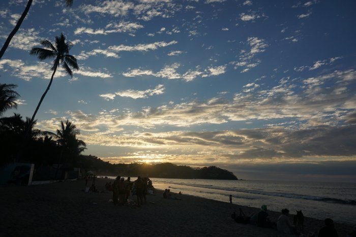Syulita beach at sunset surroundeed by palm trees with people sitting along the sandy shore