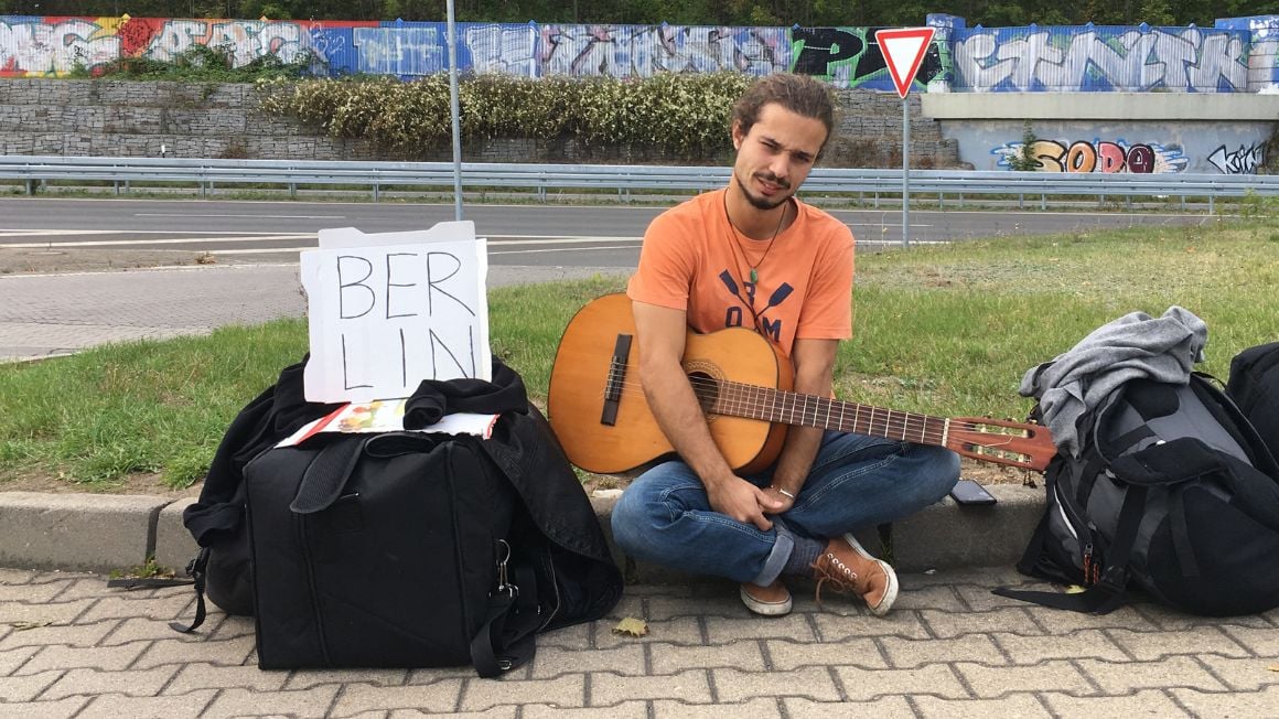 young musician with guitar waiting to hitch a ride to berlin