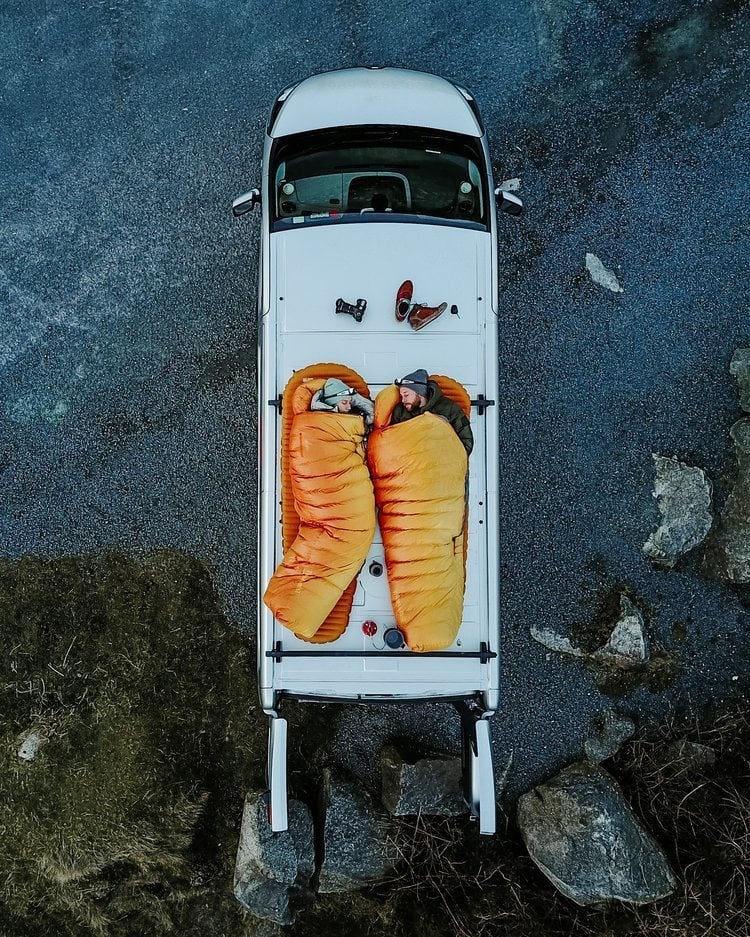 Two travellers in sleeping bags on top of their van in oceania
