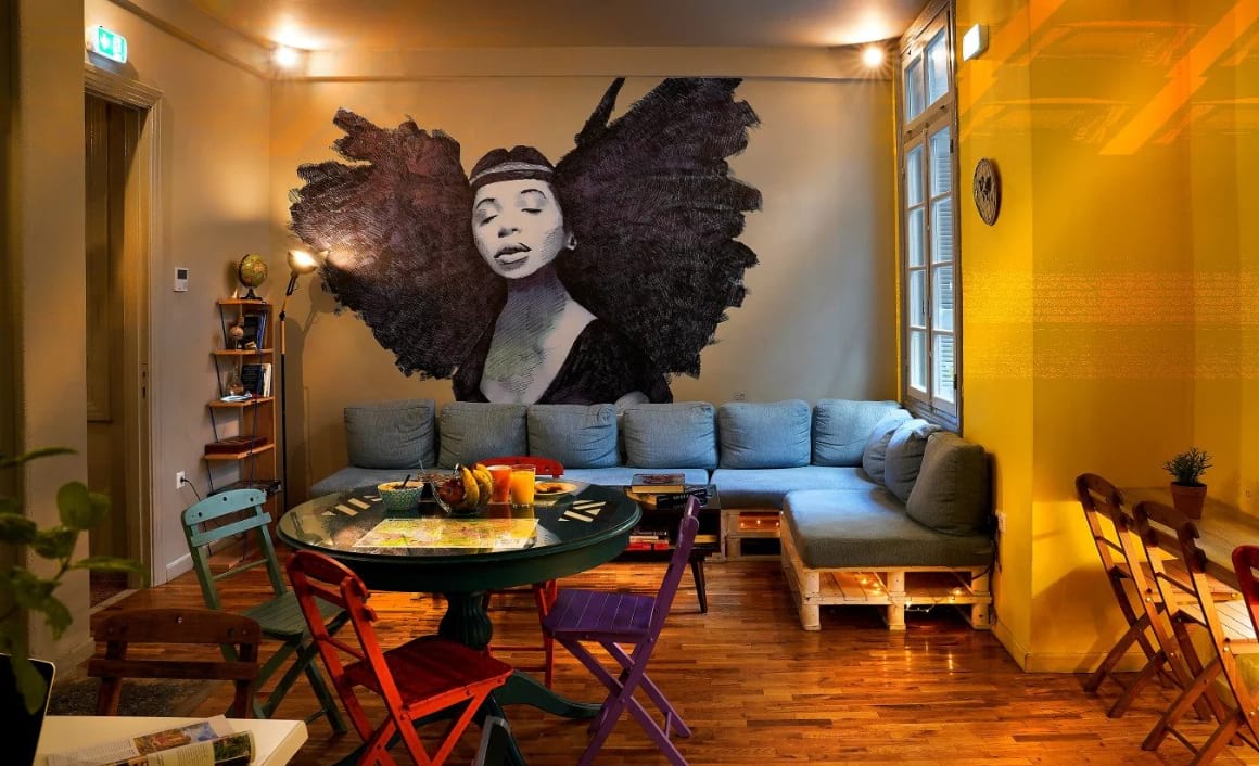 Shared space in hostel with large artwork on the wall, comfy pallet sofa and table and chairs