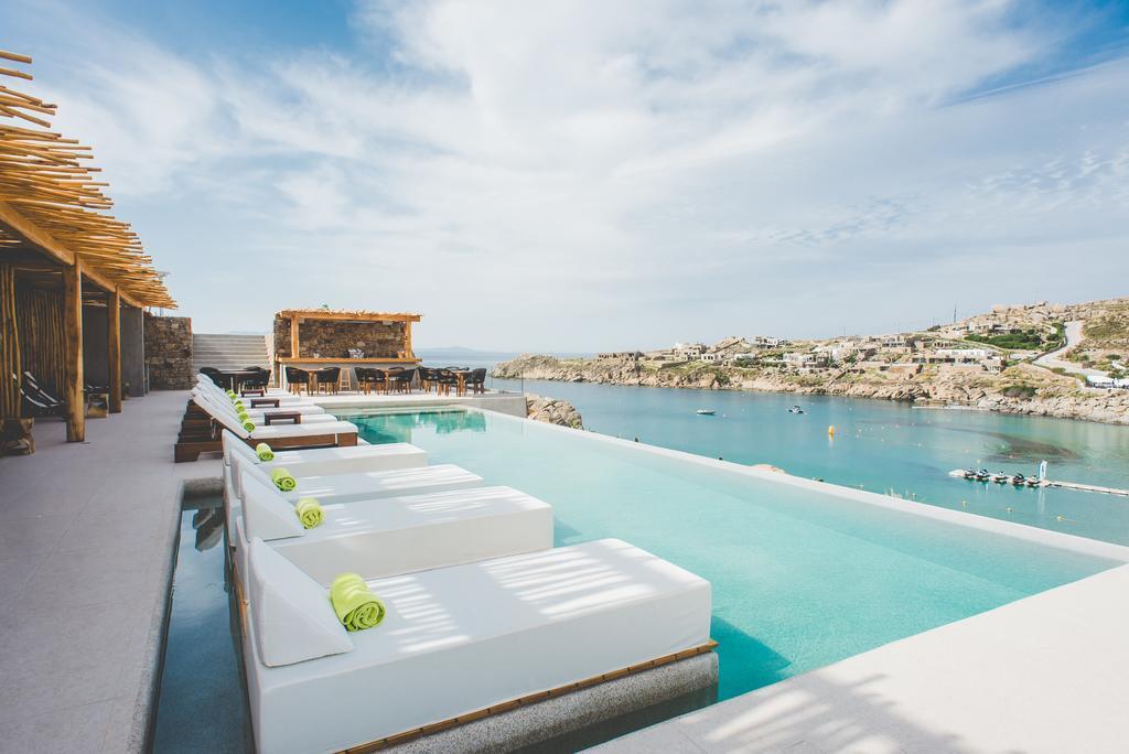 Hostels in Mykonos with sunloungers in an infinity pool on the sea with golden sand cliffs in the background