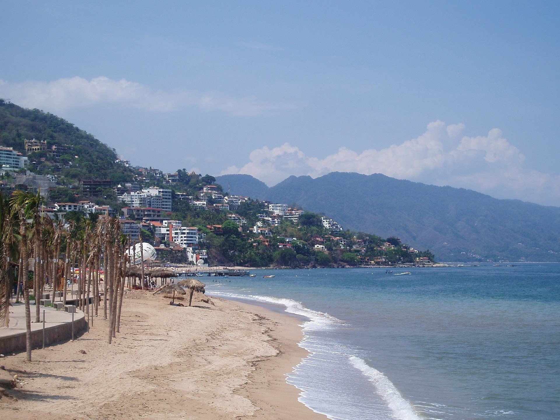 View along the beach at Hotel Zone on a clear day with houses on a hill in the background.