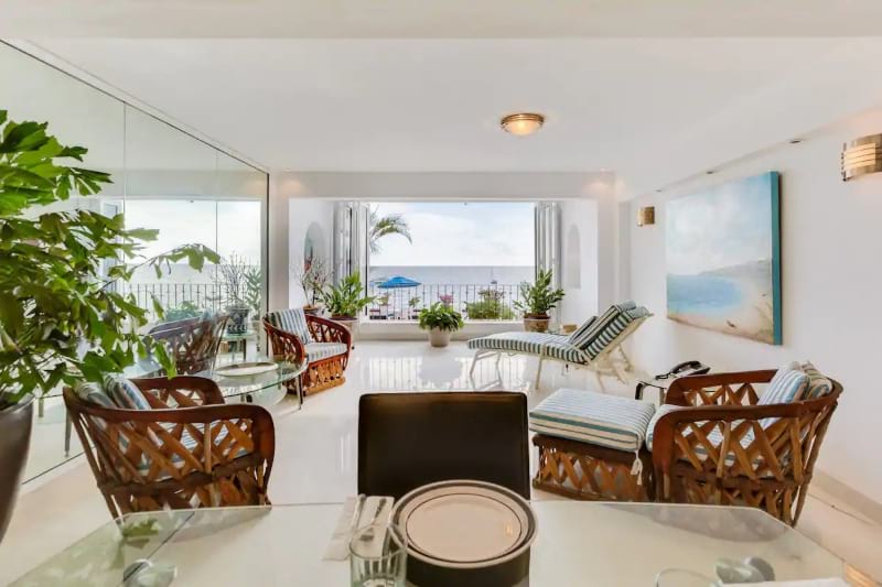 Stunning, white walled lounge area with couches and pot plants. The end of the room has a big window showing a view of the ocean.