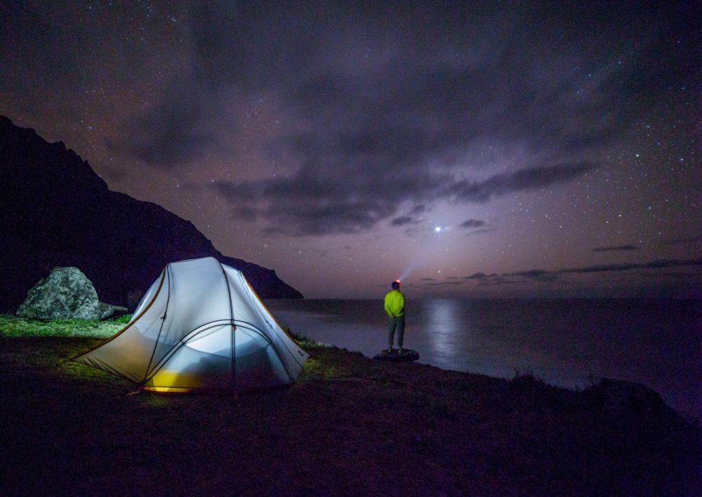 A camper watches a sky full of stars with their tent set up behind them. 