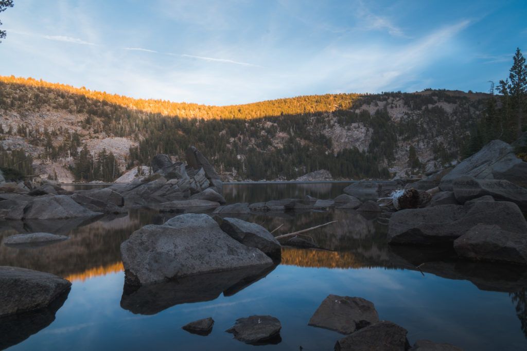 A rocky forested landscape behind a lake at sunset in California