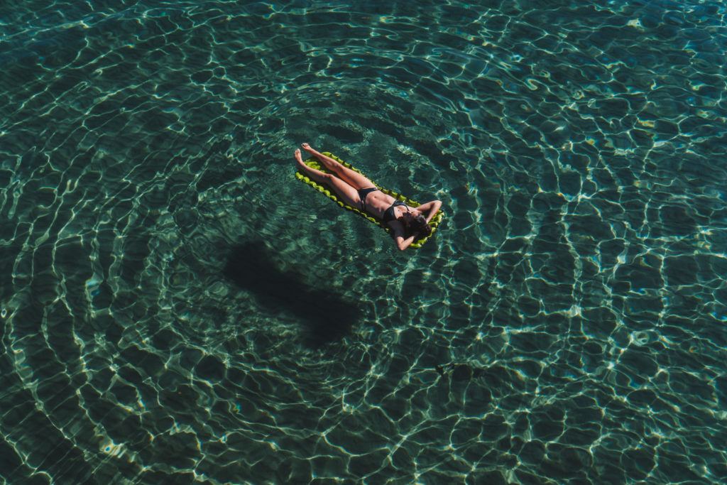 Girl floating in blue water taking a break from travelling too much
