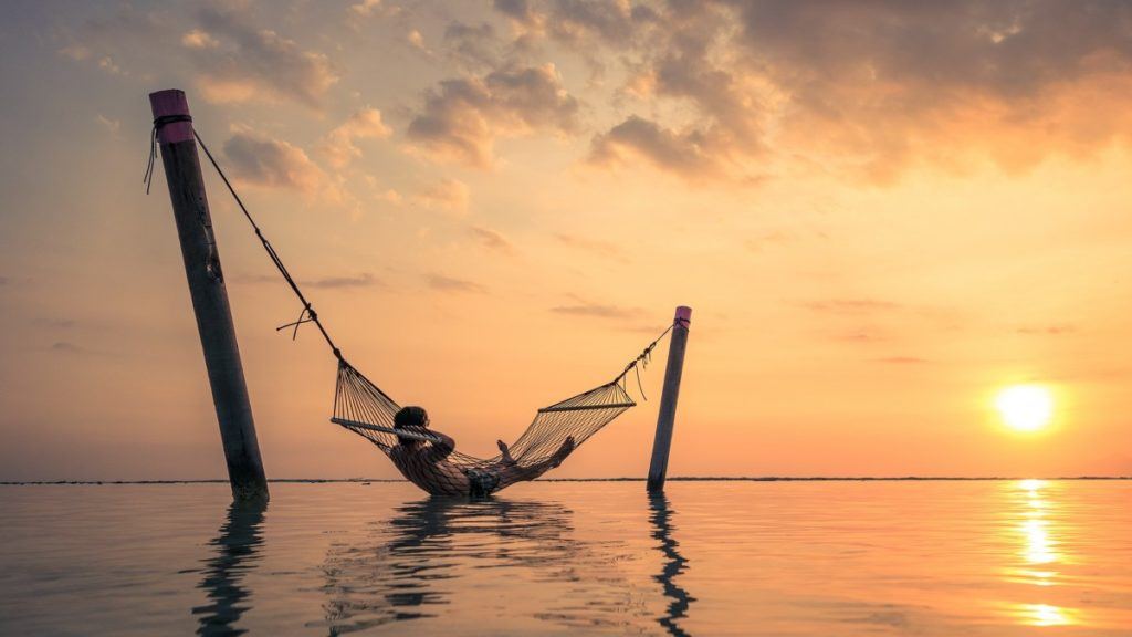 a man lies in a hammock over the water at sunset in bali