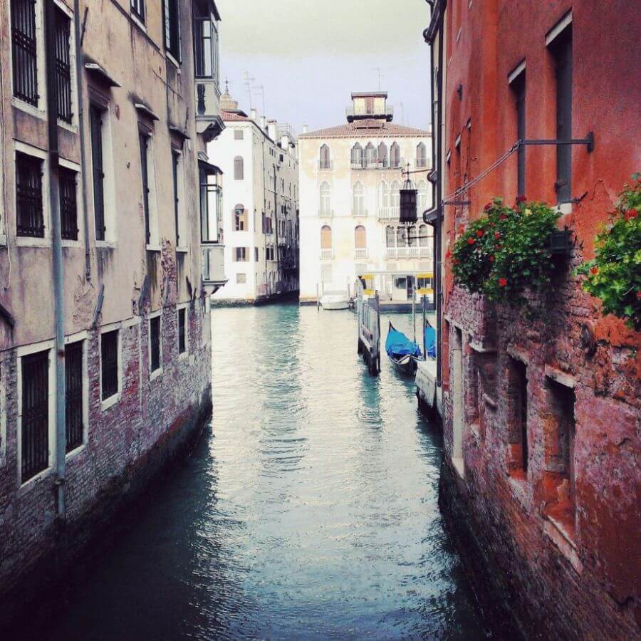 A canal in Venice Italy flanked by old brick buildings and one gondola in sight
