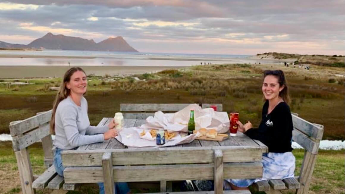 dani and friend having fish and chips by the beach north of auckland, new zealand