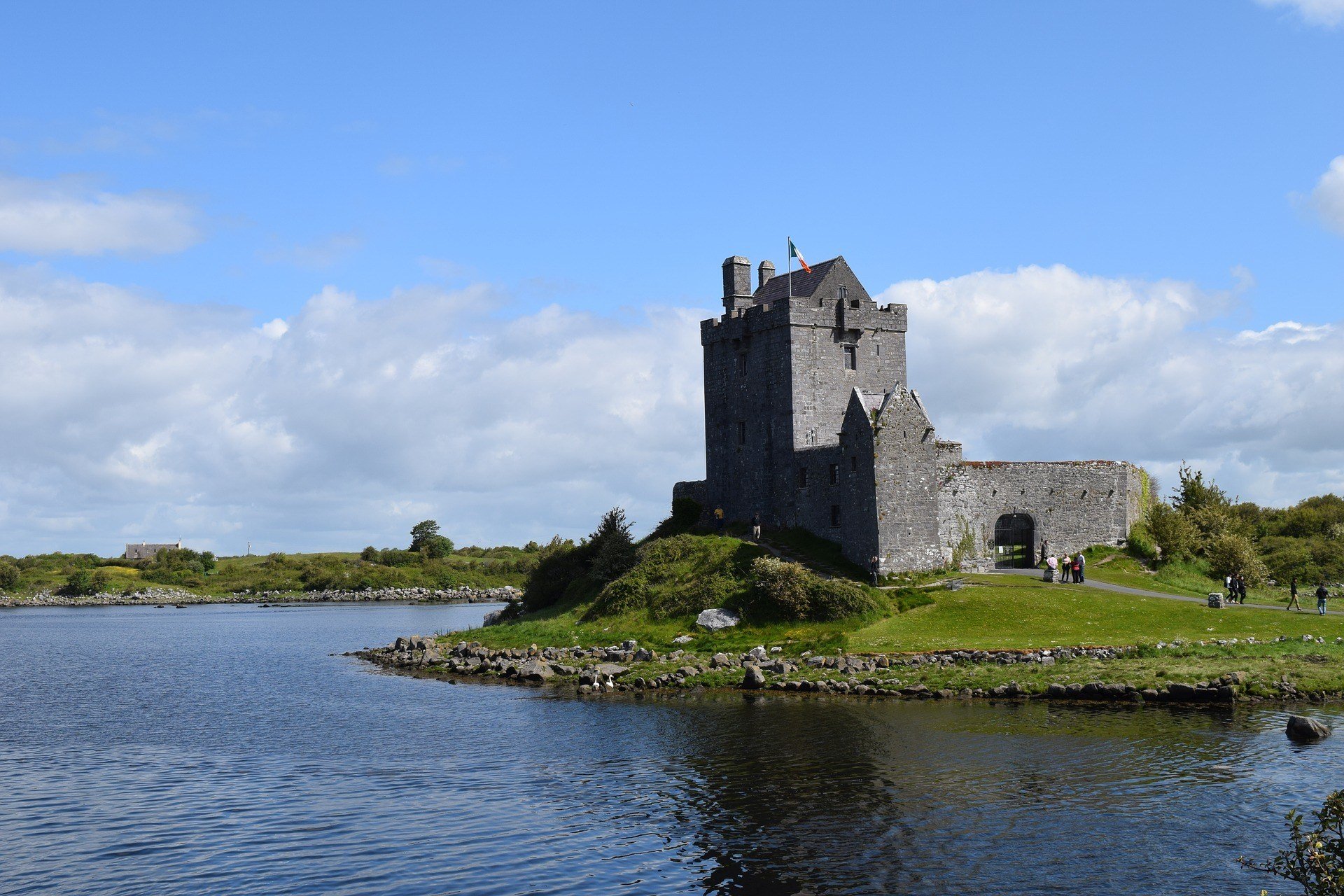 View over the water to an old, grey, stoney building. Beautiful blue sky day.