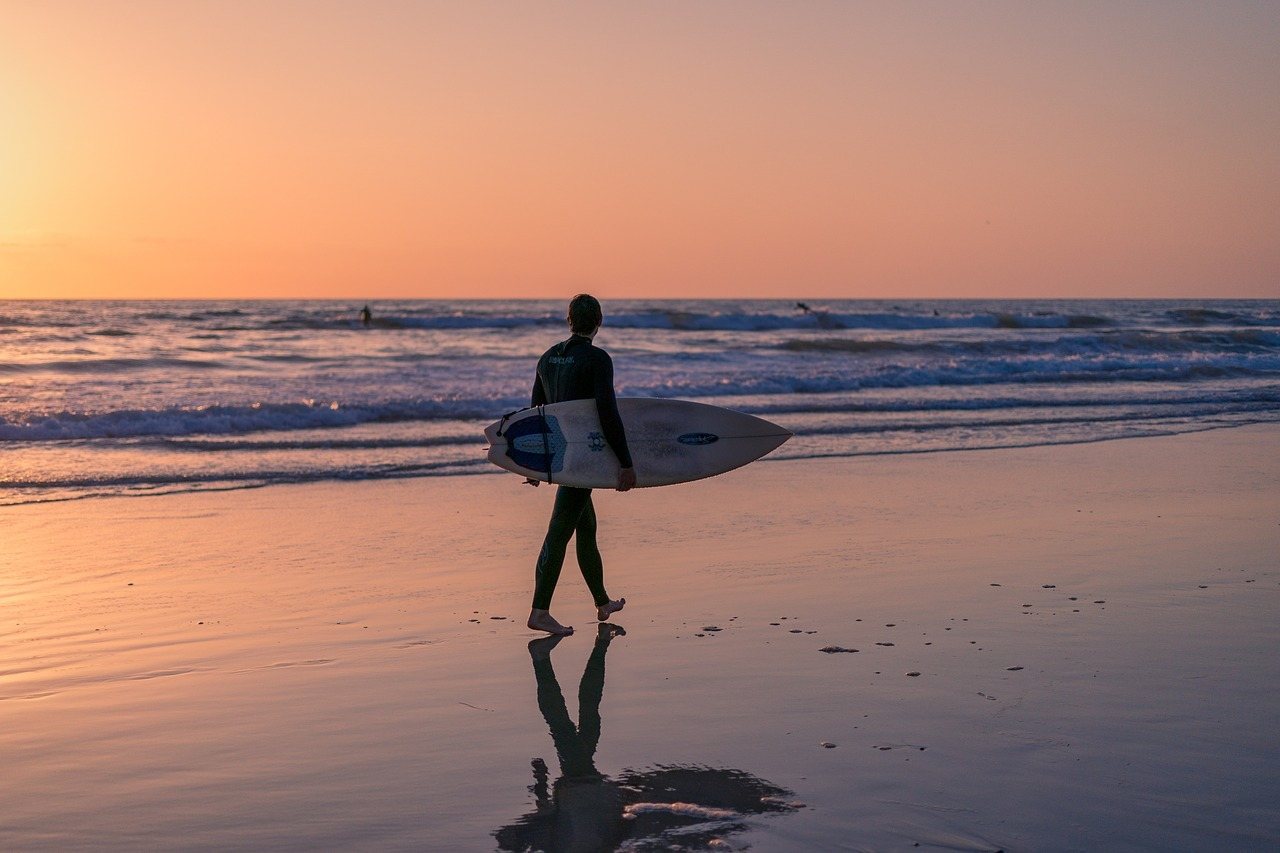 surfer walking beach at sunset in california