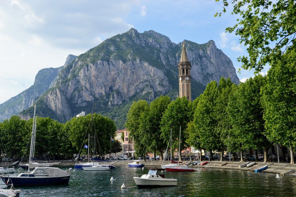 Lake Como with sailboats in the foreground and a clocktower and mountains in the background