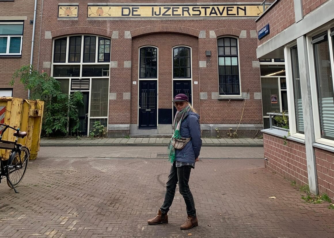 Laura wearing lots of warm clothes in front of a typical Dutch building on a quiet Amsterdam road