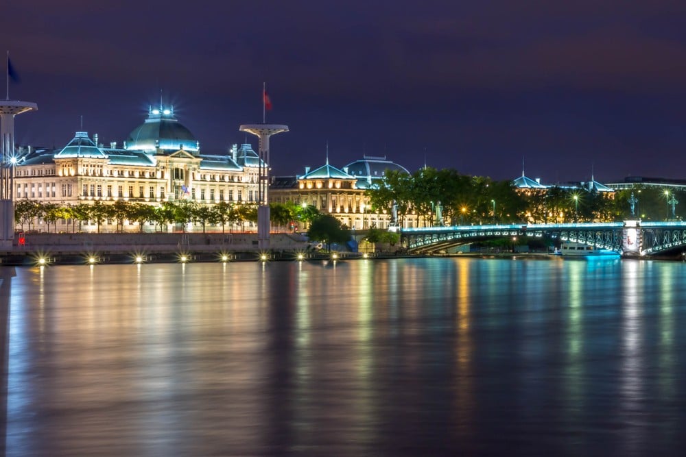 La Guillotiere, Lyon at night time. View from across the river with the bridge and buildings lit up in blue light.