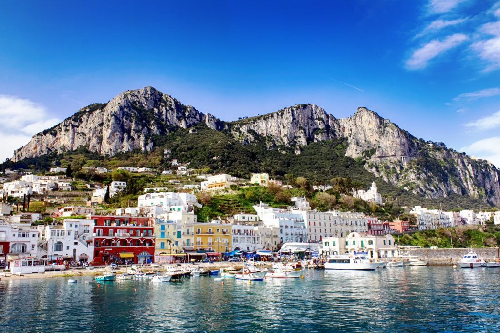 harbor view of Marina Grande, Capri, Italy with buildings and boats at the coastline and mountains in the background
