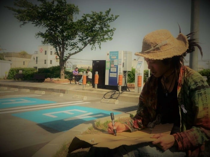 A Japanese backpacker writes a hitchhiking sign in Kanji before the day's travels