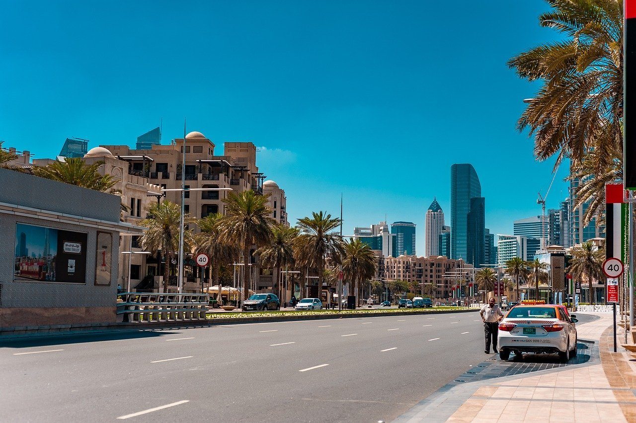 A taxi in a large street in Dubai with buildings and palm trees  