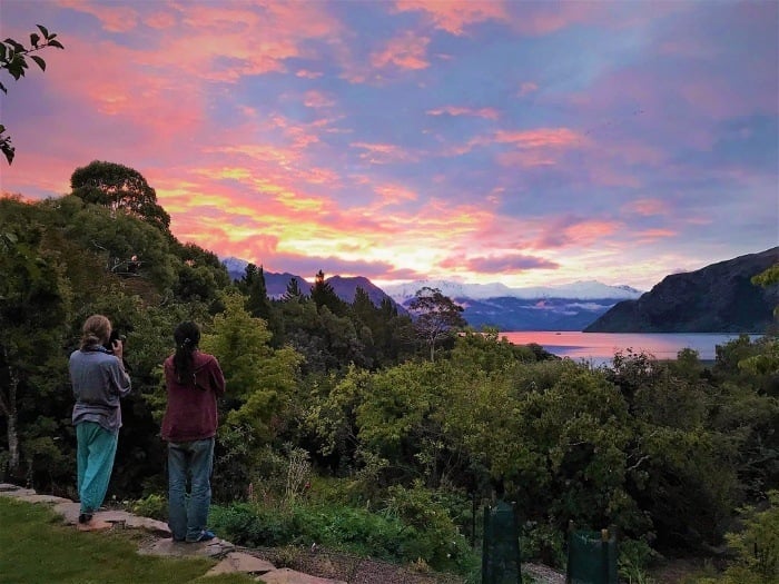 two backpackers watching a colorful pink orange and purple sunset while traveling in wanaka new zealand