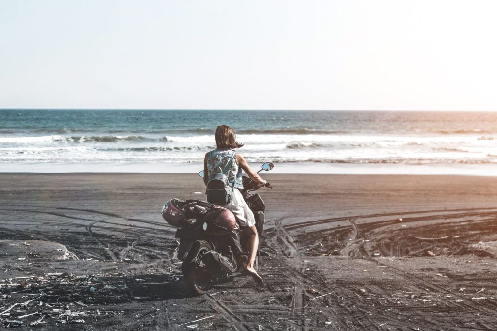 Young woman driving a scooter at the beach with black sand Bali Indonesia.