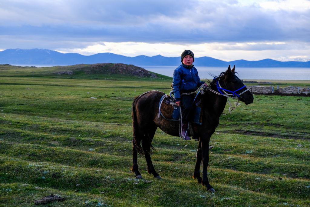 young child riding a horse in kyrgyzstan with a blue lake in the background