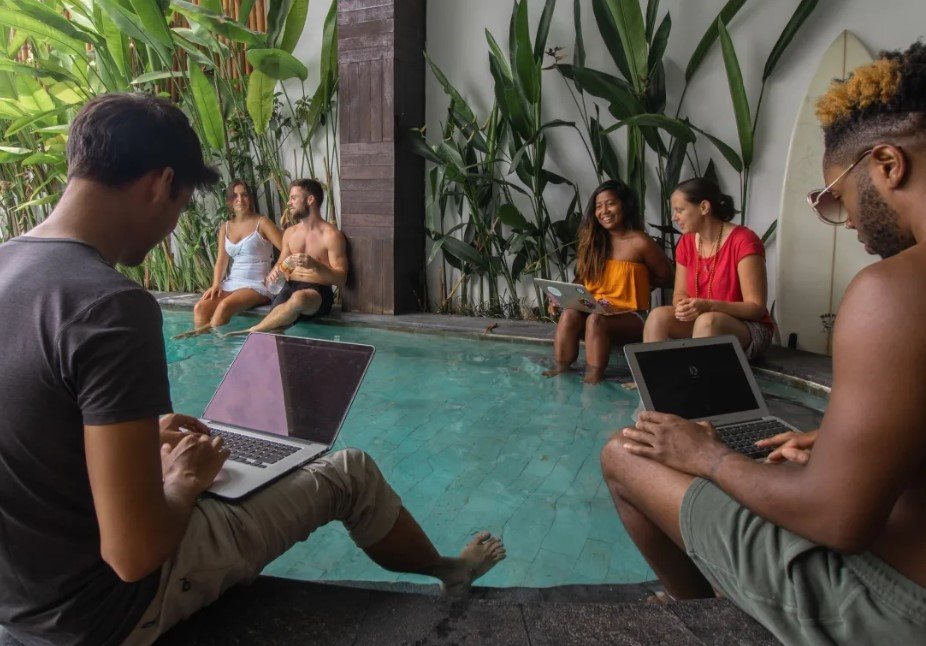 people sitting around the pool deing digital nomads co working on laptops at Draper House