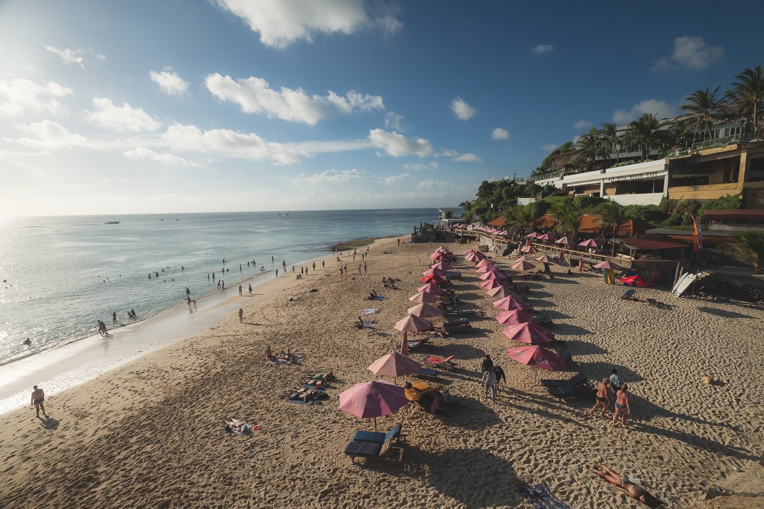 Rows of pink beach umbrellas on a sunny day at Dreamland Beach in Uluwatu